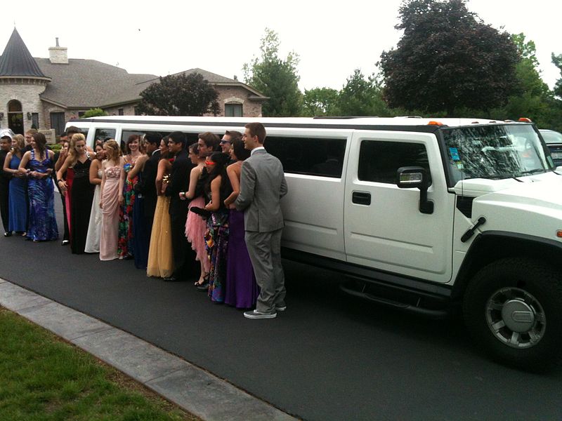 prom students taking picture next to limousine party bus